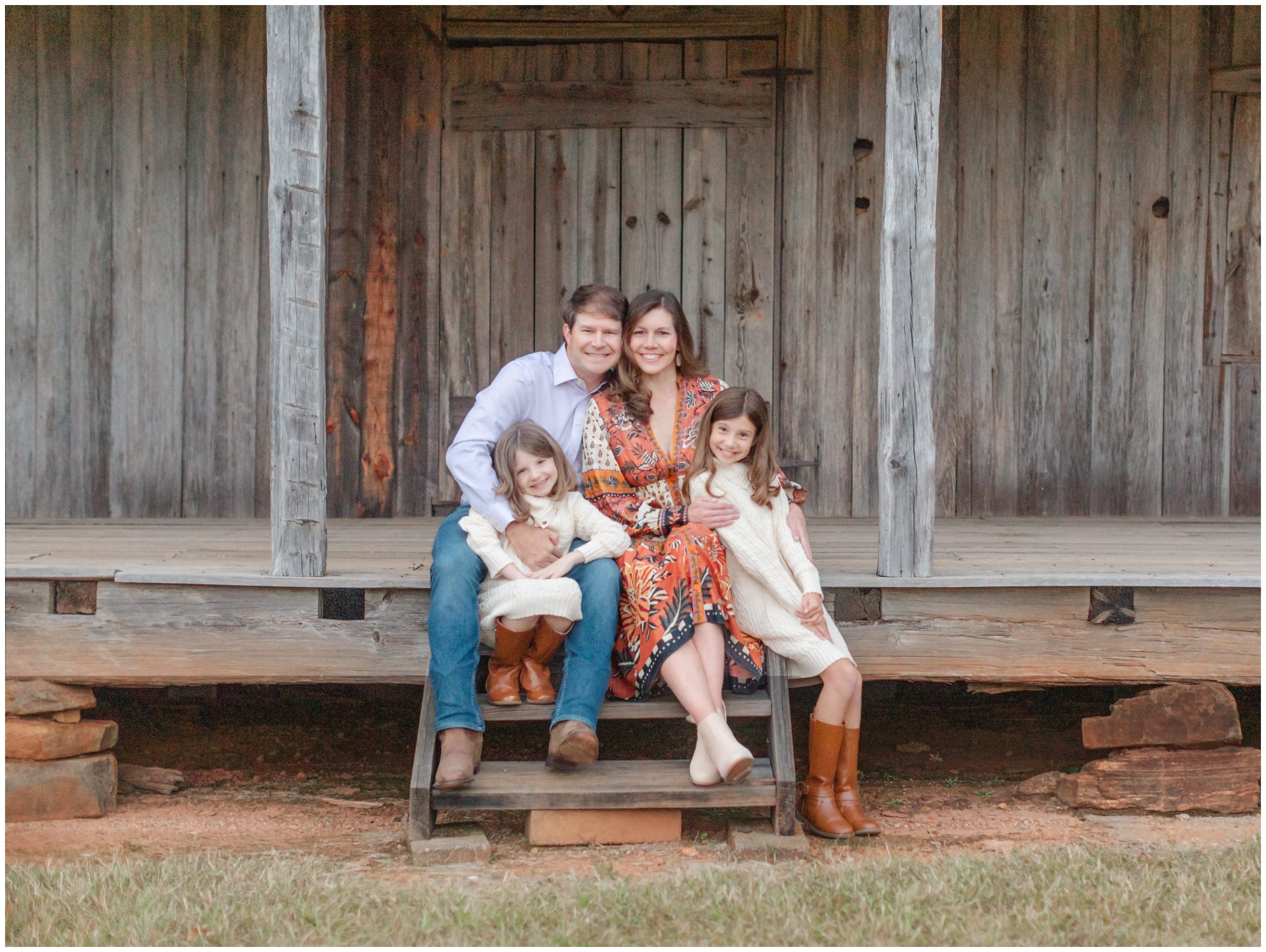 Family of four sitting together on a rustic cabin porch during fall portraits