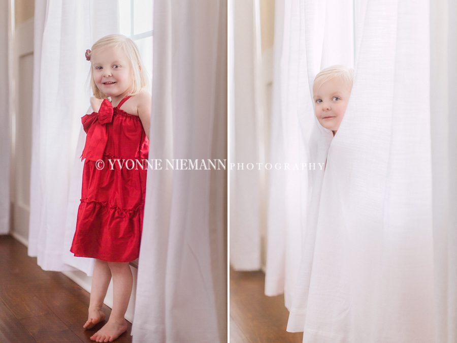 Little girl in red dress playing peek a boo behind curtains at her home in Bishop, GA.