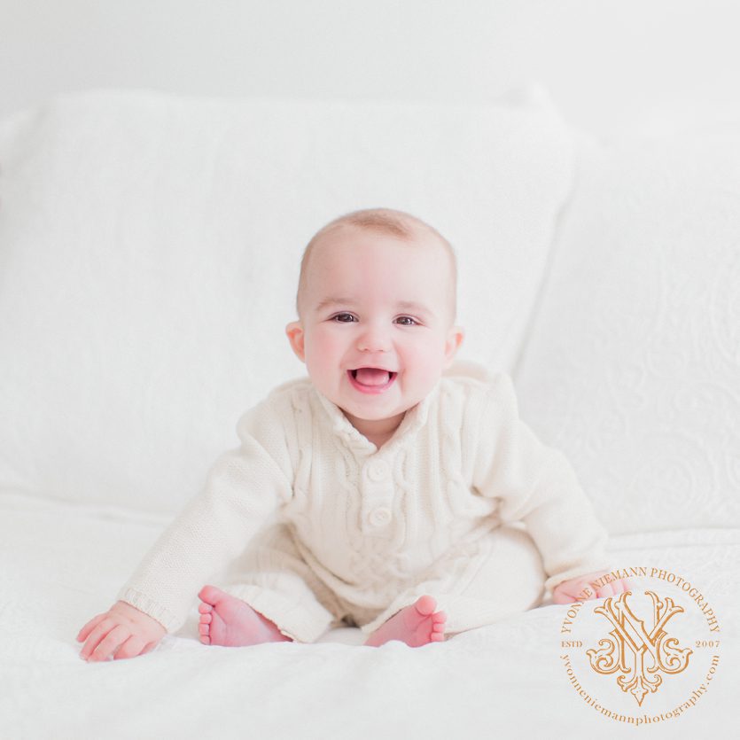 six month old baby boy sitting on bed all in white taken by Yvonne Niemann Photography in Athens, GA.